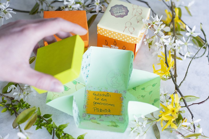 Geöffnete Explosionsbox mit Gutschein für ein Picknick.