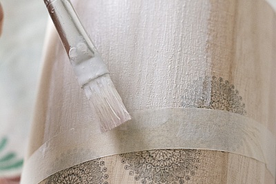 Pinsel trägt weiße Farbe auf abgeklebte Holzfläche auf