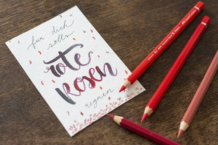 Eine geletterte Karte "Für dich solls rote Rosen regnen" und rote Buntstifte auf einem Tisch 