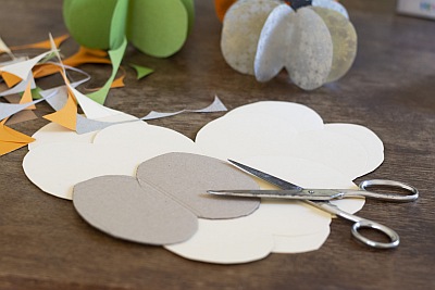 Schablone zum Basteln eines Papierkürbisses liegen ausgeschnitten auf einem Tisch. Im Hintergrund sind fertig gebastelte Kürbisse zu sehen.