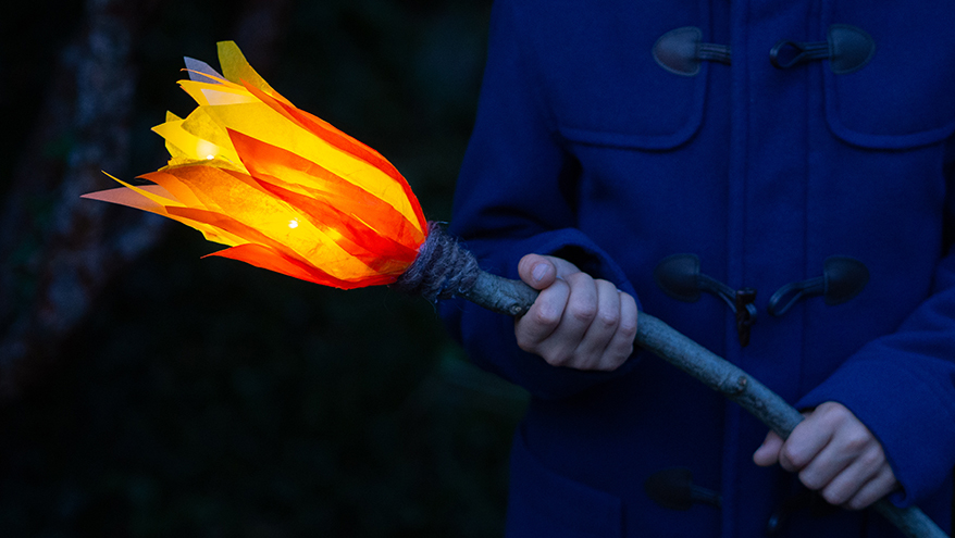 Eine Person mit blauen Mantel hält eine hell erleuchtete LED-Fackel aus PET-Flaschen in der Hand.