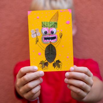 Kind hält herbstliche Bastelkarte mit Monster aus Blättern hoch