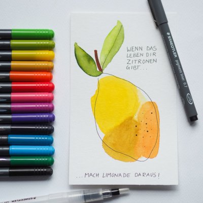 Aquarellkarte mit Motiv einer Zitrone, daneben bunte Brush Pens