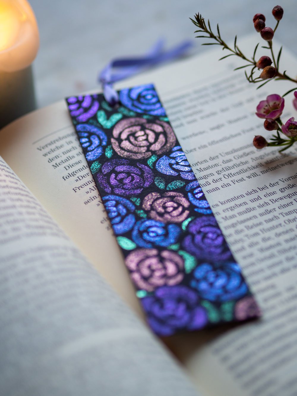 Schimmerndes Lesezeichen mit Rosenmotiv auf einem aufgeschlagenen Buch.