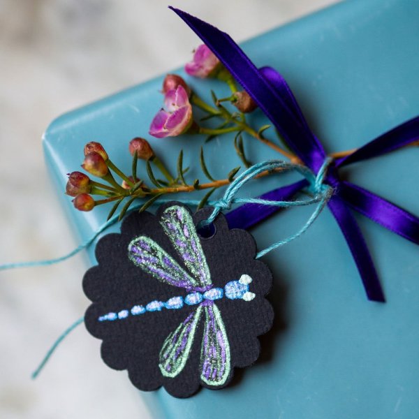 Nahaufnahme eines Geschenks mit schwarzem Anhänger und bunter Libelle