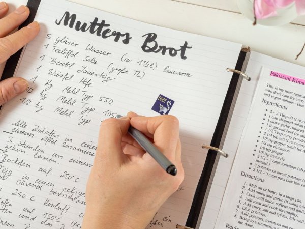 Hand schreibt Rezept für Mutters Brot in Meal-Prep-Planer