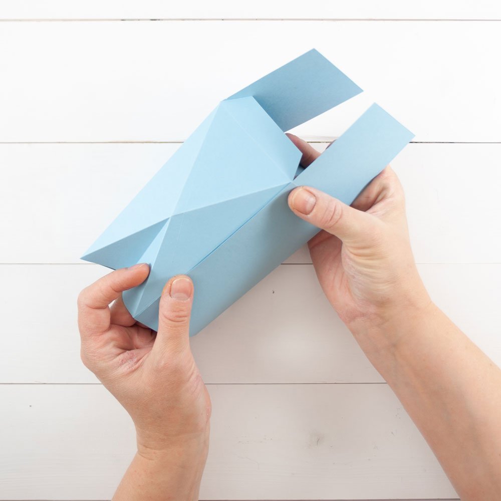 Zwei Hände kleben eine ausgeschnittene Schachtel zusammen.