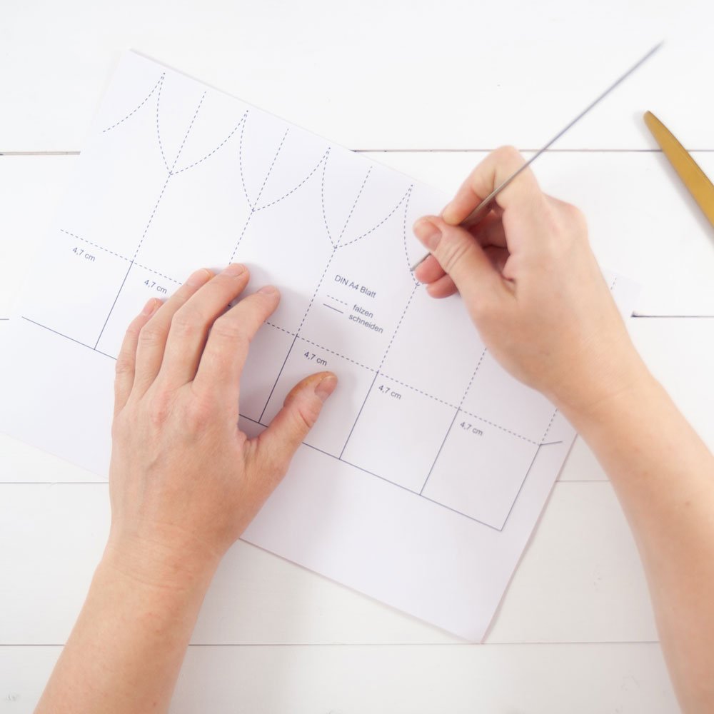 Zwei Hände übertragen Striche von einer Bastelvorlage auf Papier.