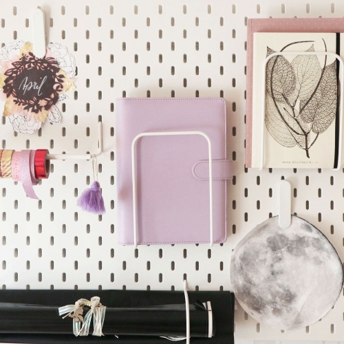 An einer Lochwand sind Notizbücher, ein Filofax-Kalender und diverse Bastelmaterialien aufgehängt.