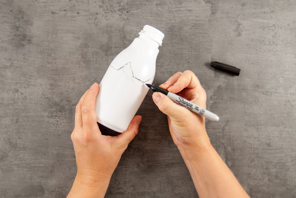 Eine Hand malt auf eine weiße Flasche Umrisse