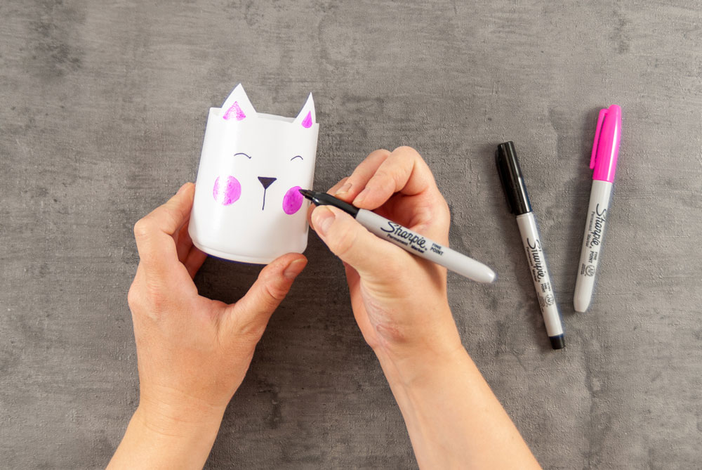 Eine weiße, zerschnittene PEF-Flasche wird mit einem Katzengesicht bemalt.