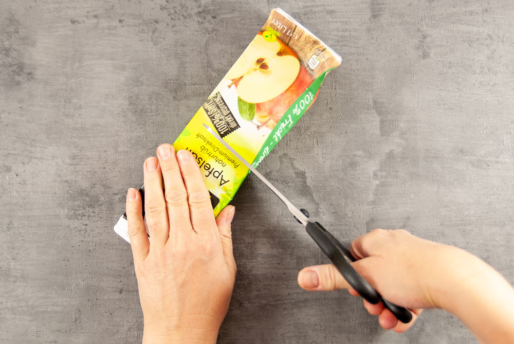 Eine Hand zerschneidet einen Getränkekarton 