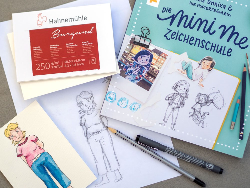 Buch Mini-Me-Zeichenschule, Hahnemühle Papier und Illustration einer Frau liegen auf einem Tisch