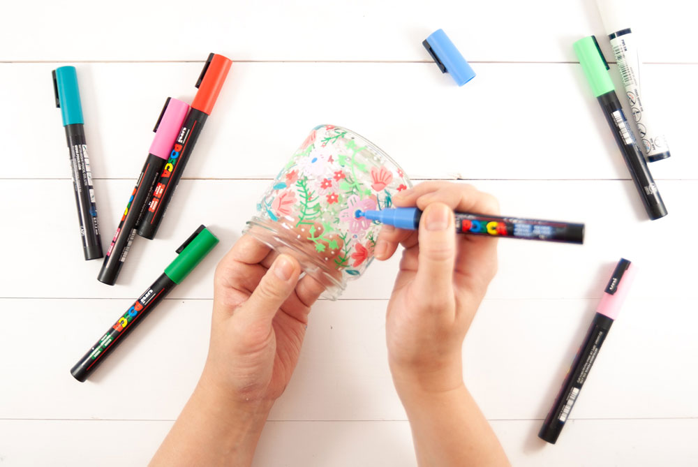 Ein Glas wird mit bunten Acryl-Farbmarkern bemalt.