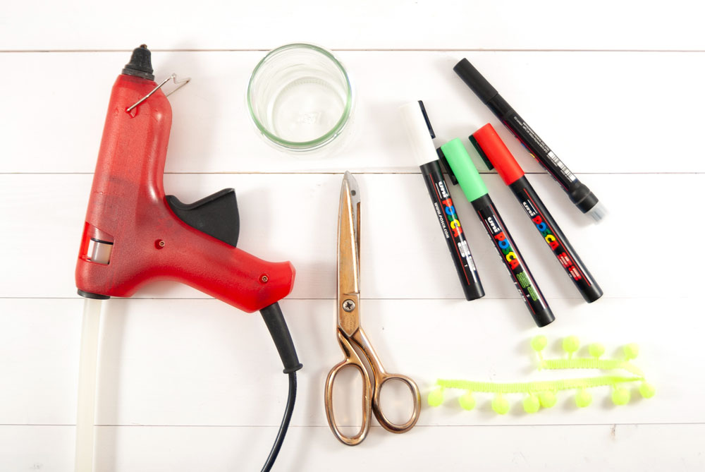 Heißklebepistole, Scheren, Glas und bunte Stifte liegen auf einem Tisch