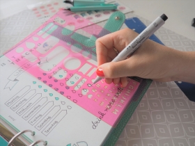 Hand nutzt pinke Schablone zum Ausfüllen eines Habit Trackers.