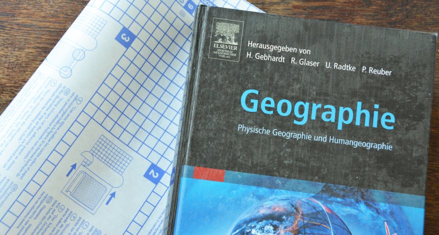 Geographiebuch und Selbstklebefolie zum Einbinden auf einem Tisch