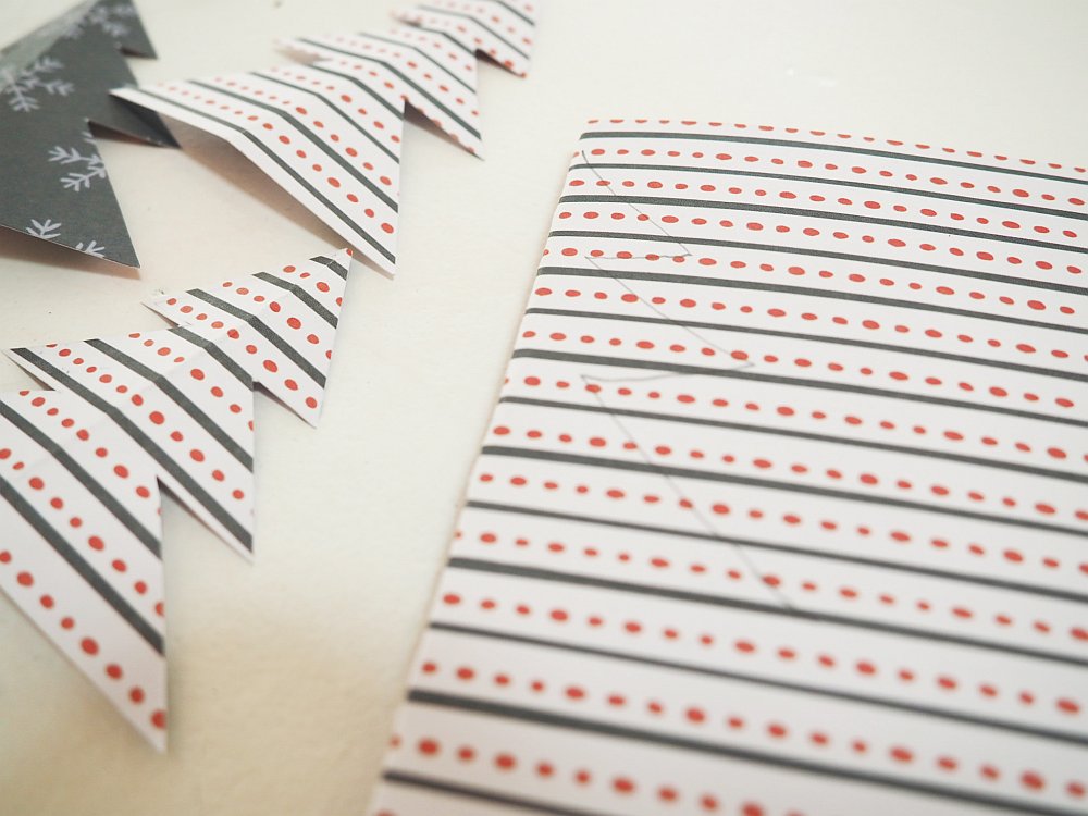 Nahaufnahme von gefaltetem Bastelpapier mit Weihnachtsmuster und Papier-Tannenbäumen.