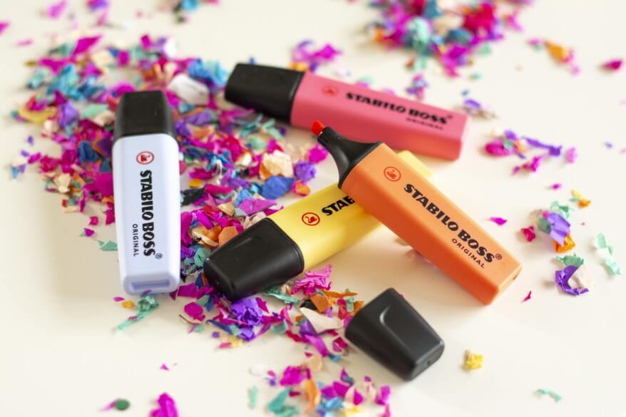 Mehrere bunte Textmarker von Stabilo liegen auf einem mit Konfetti bestreuten Tisch.