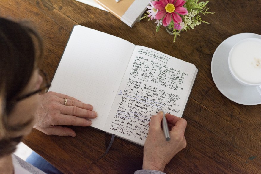 Eine Person schreibt in ein Notizbuch, daneben steht Kaffee.