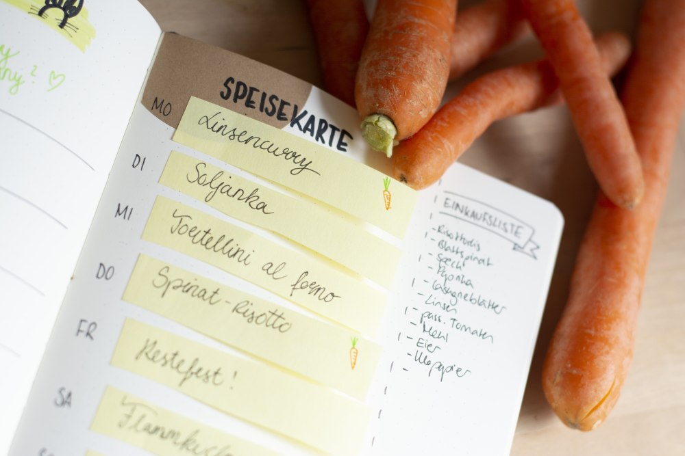 Speiseplan mit Post-its im Bullet Journal, daneben frische Karotten