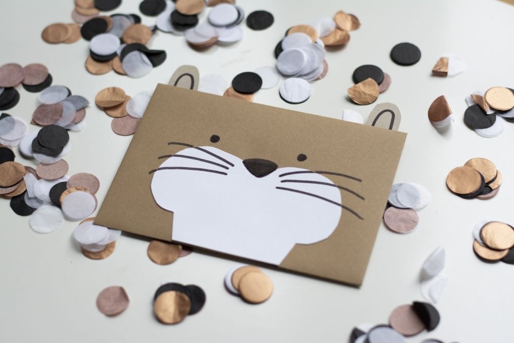 Einladungskarte zum Kindergeburtstag: Selbst gebastelte Do it yourself-Karte Otter liegt auf Konfetti.
