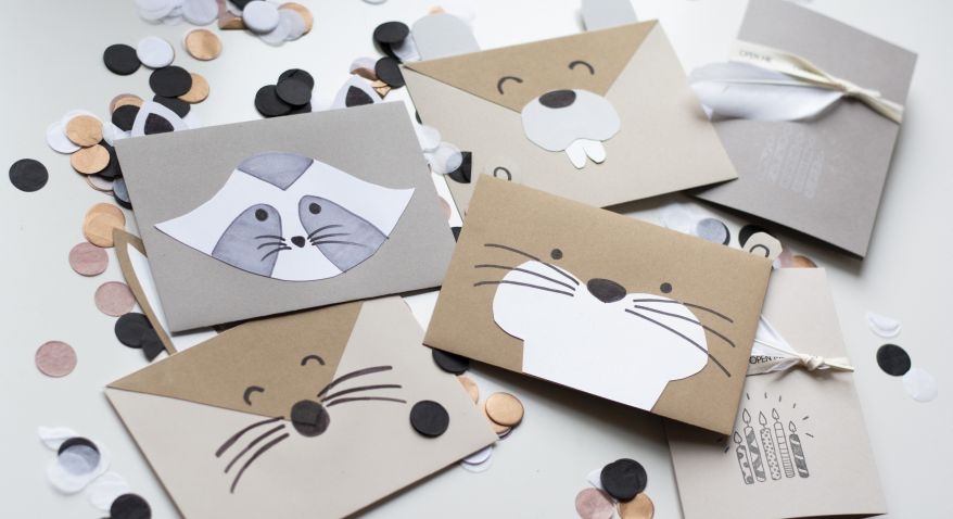 Einladungskarten zum Kindergeburstags als Waldtiere. Selbst gebastelte Briefumschläge in Form von Otter, Biber, Waschbär und Hase liegen auf Konfetti.