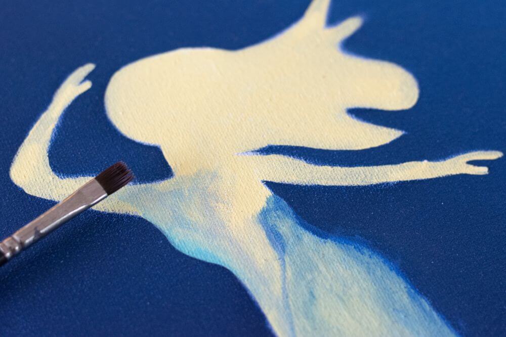 Nahafufnahme einer gemalten Meerjungfrau aus Acryl. Mit einem Pinsel wird hellblaue Farbe verteilt, um die Farben zu verblenden.