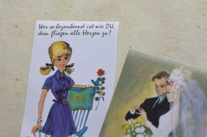 Detailaufnahmen historischer Glückwunschkarten zu Geburtstag und Hochzeit von ABC cards. Auf der Geburtstagskarte steht geschrieben "Wer so bezaubernd ist wie du, dem fliegen alle Herzen zu".