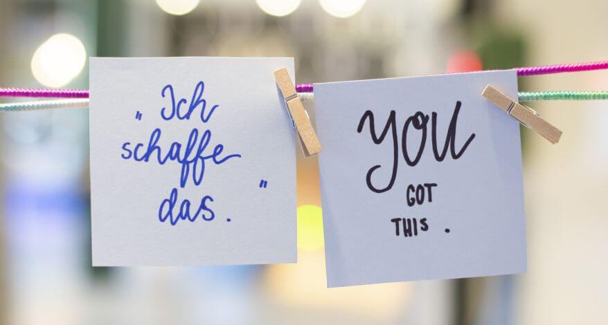 An zwei gespannten Fäden in grün und rosa wurden zwei Notizzettel mit Klammern aus Holz befestigt. Darauf sind zwei Mantras gegen Prüfungsangst zu lesen: "Ich schaffe das." und "You got this."