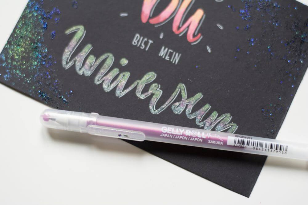Nahaufnahme eines selbstgemachten Handletterings "Du bist mein Universum", das mit Gelstiften "Gelly Rolls" von Sakura gestaltet wurde. Das Wort "Universum" glitzert, da es mit den Stiften "stardust" von Sakura geschrieben wurde.