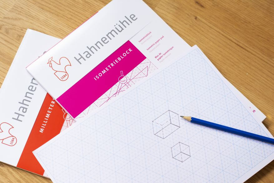 Zwei Zeichenblöcke (Isometrieblock und Millimeterblock) von Hahnemühle liegen auf einem Tisch, darauf liegt ein Blatt Papier mit der Zeichnung von zwei geometrischen Körpern für den Mathematikunterricht.