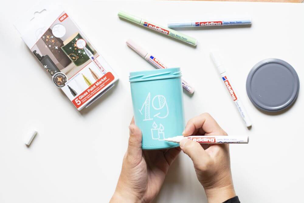 Anleitung Upcycling-Adventskalender aus Glas basteln, Schritt 2: Besprühte Marmeladengläser mit Glanzlackmarkern mit den Ziffern 1 bis 24 beschriften.