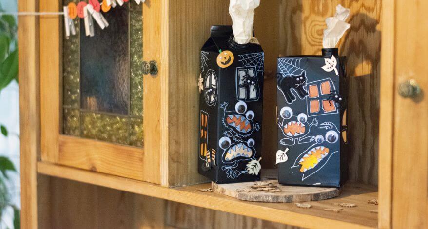 Bunt bemalte Milchtüten mit Halloween Motiven stehen in einem Holschrank zur Deko.