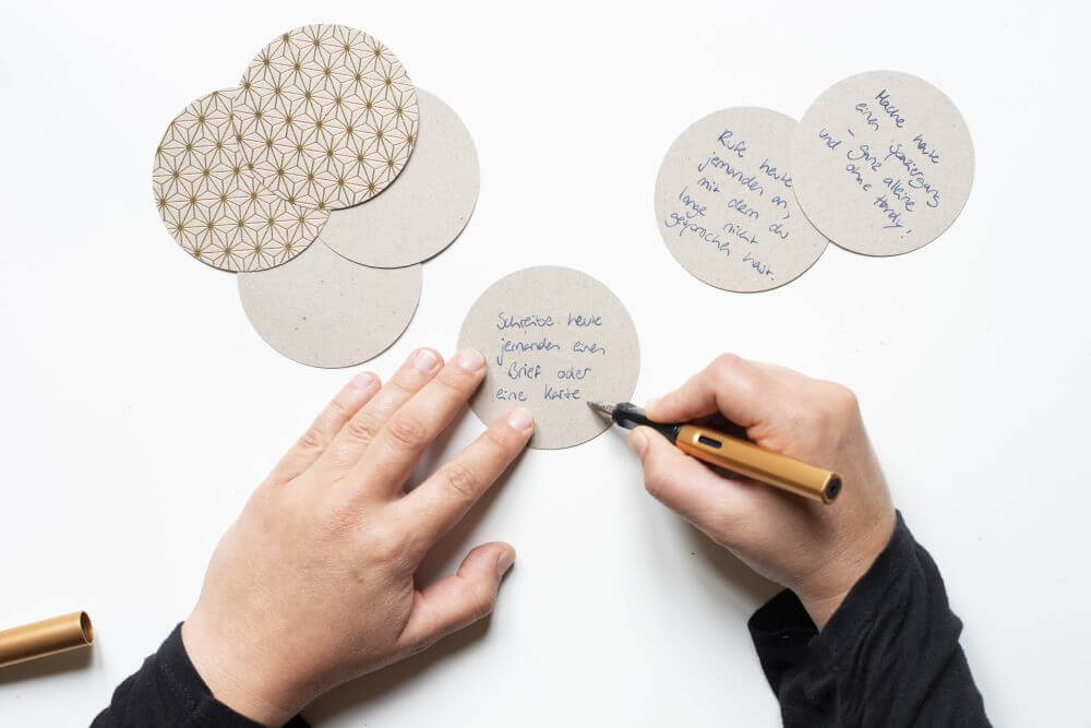 Eine Hand beschriftet Motivpapier in kreisform mit verschiedenen Sprüchen mit Hilfe eines goldenen Füllers.