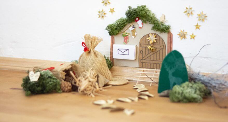 An einer Wand sieht man eine selbstgebastelte Wichteltür, die mit verschiedenen Bastelmaterialien (zum Beispiel Islandmoos, Jutesäckchen, Sticker und Stempel) von Knorr Prandell und Heyda dekoriert wurde. 