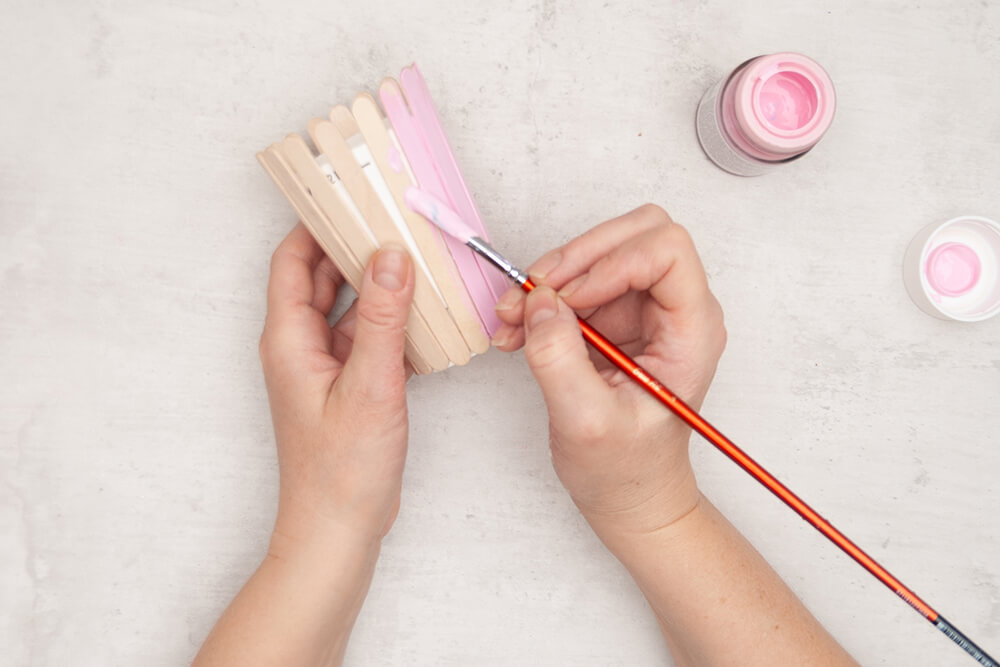 Ein Pappbecher mit aufgeklebten Bastelhölzern von Knorr-Prandell wird mit Rosa Acrylfarbe angemalt. Fotos: Johanna Rundel