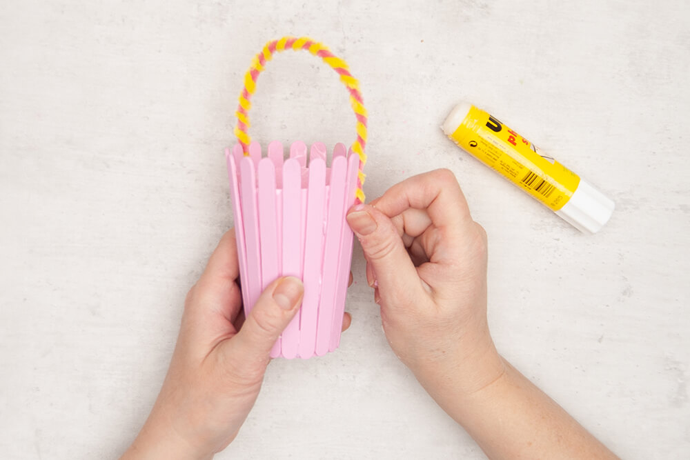 Ein Chenilledraht von Knorr-Prandell wird als Henkel an einen rosafarbenen Pappbecher mit Bastelhölzern geklebt. Jetzt ist es ein Osterkörbchen. Fotos: Johanna Rundel