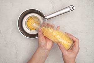 Jemand gibt eine Tüte Bienenwachspastillen von Knorr-Prandell in eine leere Konservendose, die in einem Wasserbad in einem kleinen Topf steht. Foto: Johanna Rundel