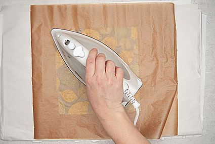 Ein quadratisches Stück gemusterter Stoff wird zwischen zwei Lagen Backpapier gebügelt, um Bienenwachs von Knorr Prandell auf dem Stoff zu verteilen. Foto: Johanna Rundel