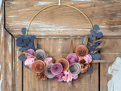An einer rustikalen Holztür hängt ein goldener Kranz mit verschiedenen Papierblumen in gedeckten Farben von Rosa bis Rost. Für die Herstellung der Blumen wurden Papiere der Firma Artoz verwendet. Foto: Johanna Rundel