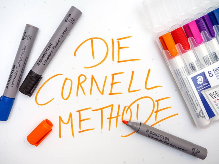 Auf einem Bogen Flipchart-Papier liegen verschiedene Stifte der Marke Staedtler. Verschiedene Lumocolor Whiteboard Marker liegen in ihrer Verpackung daneben. Auf dem Papier steht in oranger Schrift: Die Cornell Methode.