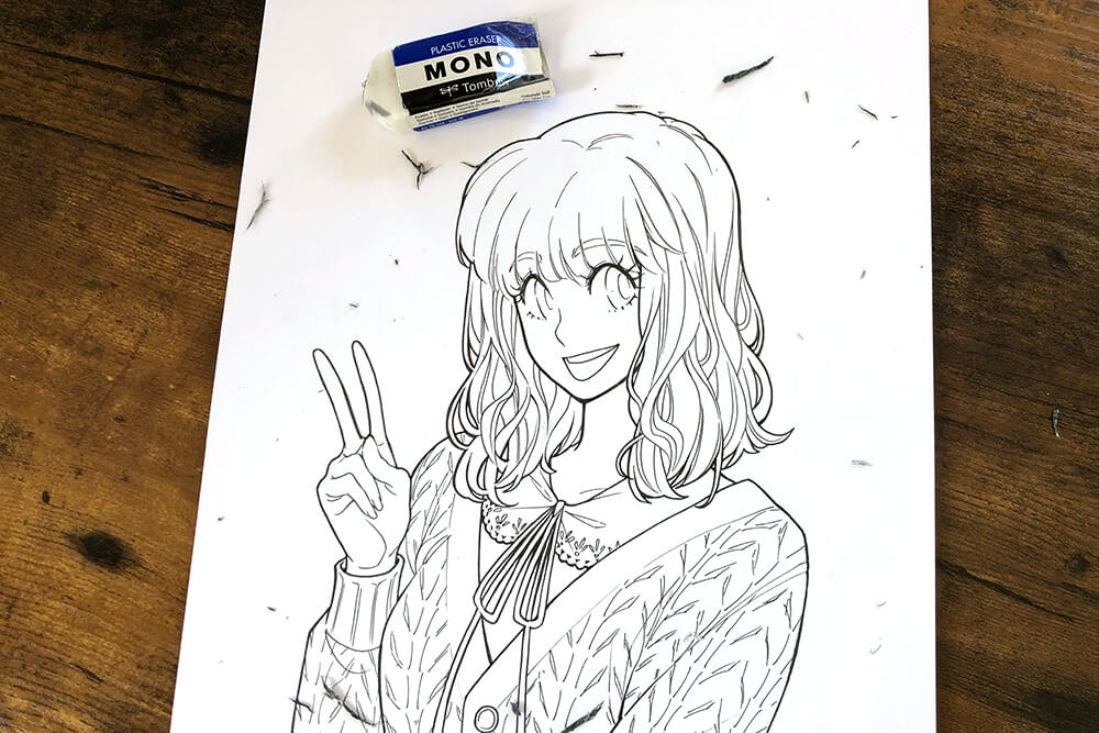 Auf einem braunen Holztisch liegt ein Blatt Papier. Darauf ist die Skizze einer jungen Frau im Manga-Stil mit Finelinern nachgezeichnet zu sehen. Mit dem MONO Radierer von Tombow wurde die Bleistiftskizze darunter wegradiert. Foto: Reyhan Yildirim