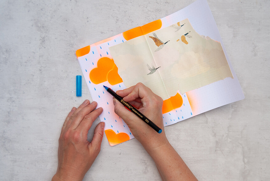 Jemand malt mit einem hellblauen Brushpen von Edding Regentropfen in ein Art Journal im Mixed-Media-Stil. Foto: Johanna Rundel