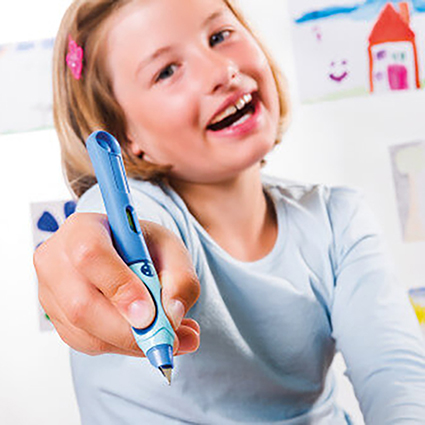 Ein Mädchen im Grundschulalter hält einen blauen Schreiblern-Füller von Pelikan in die Kamera und lacht dabei. Sie trägt ein hellblaues Longsleeve und eine rosa Spange im blonden Haar. Im Hintergrund sind selbstgemalte Bilder zu sehen.