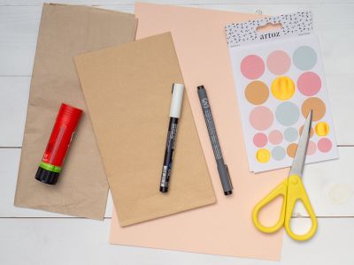 Auf einem hellen Untergrund liegen alle Bastelmaterialien, die man zu Herstellung einer Igel-Grußkarte benötigt: eine grüne Blanko Klappkarte, Stempel „Happy Birthday“´, ein schwarzes Stempelkissen von Artoz, getrocknete Herbstblätter, rosa Tonkarton, Klebestift, Marker in schwarz und weiß, Mini-Pompons, eine gelbe Schere, Klebestift und einen Stanzer. Foto: Johanna Rundel 