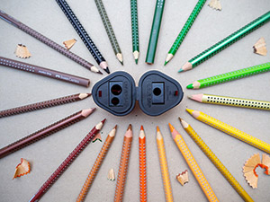 Auf einem Kraftpapier liegen viele verschiedenfarbige Buntstifte der Grip-Serie von Faber-Castell um eine geöffnete Dreifachspitzdose im Kreis. Einige Spitzreste sind dazwischen verteilt. Foto: Johanna Rundel