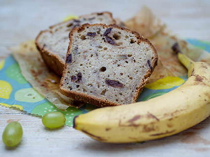 Bananenbrot auf Servietten, daneben liegt eine Banane und Trauben.