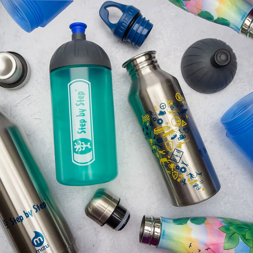 Auf einem hellgrauen Untergrund in Betonoptik liegen verschiedene Trinkflaschen von Step by Step. Teilweise sind die Verschlüsse und Deckel abgeschraubt. Foto: Johanna Rundel