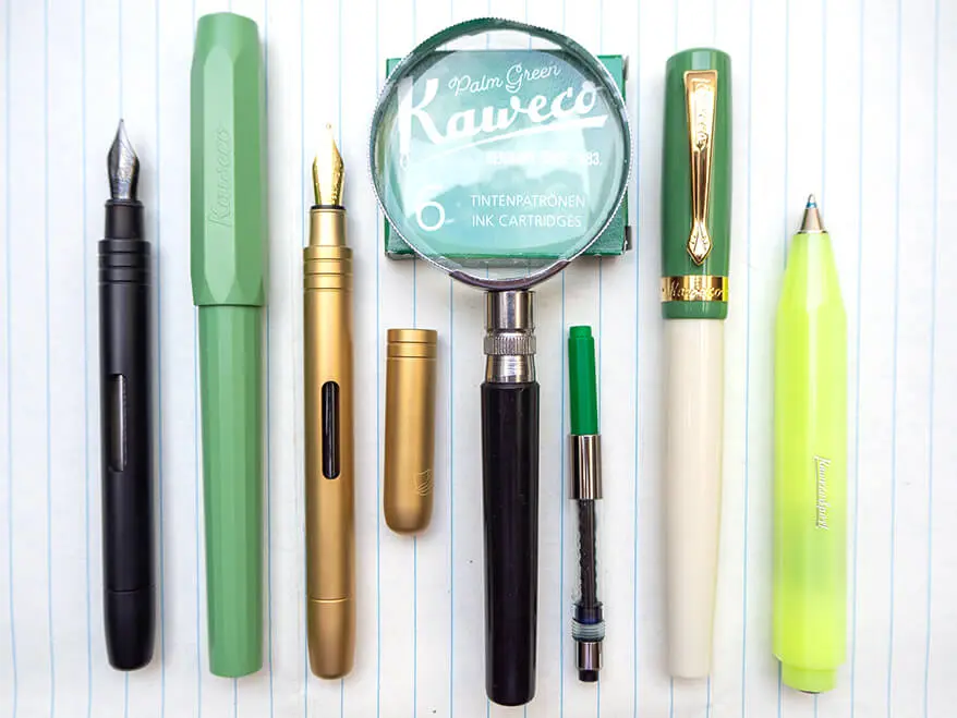 Auf einem linierten Papier liegen verschiedene Schreibgeräte von Kaweco. Von rechts nach links: Ein schwarzer Füller ohne Kappe, ein hellgrüner Füller, ein geöffneter goldener Füller, eine Packung grüne Tintenpatronen, auf denen eine Lupe liegt, ein Tintenkonverter, ein grün-beiger Füller im Retro-Stil und ein neongelber, dicker Kugelschreiber. Foto: Johanna Rundel 